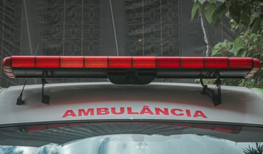 A close-up view of a city ambulance with a red siren light and Portuguese text 'AMBULÂNCIA'