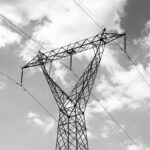 A high voltage power line towering against a dramatic cloudy sky in a black and white composition.