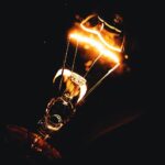 Dramatic close-up photo of an illuminated light bulb filament glowing in the dark.
