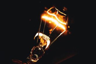 Dramatic close-up photo of an illuminated light bulb filament glowing in the dark.