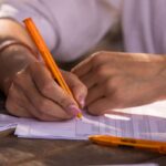 hands writing with orange pen on documents