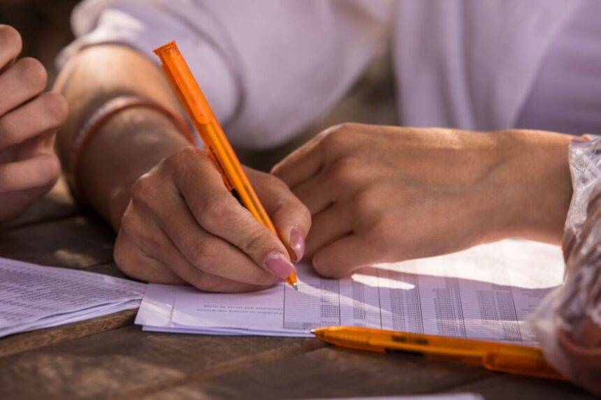 hands writing with orange pen on documents