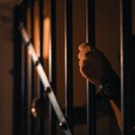 Silhouetted hand gripping jail bars, highlighting solitude and confinement.