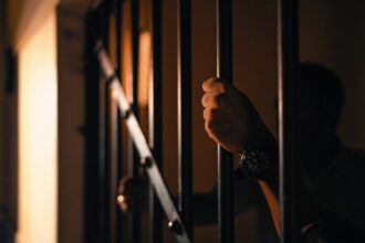 Silhouetted hand gripping jail bars, highlighting solitude and confinement.